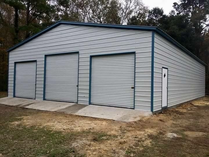 White metal garage with three blue-trimmed roll-up doors and a walk-in door